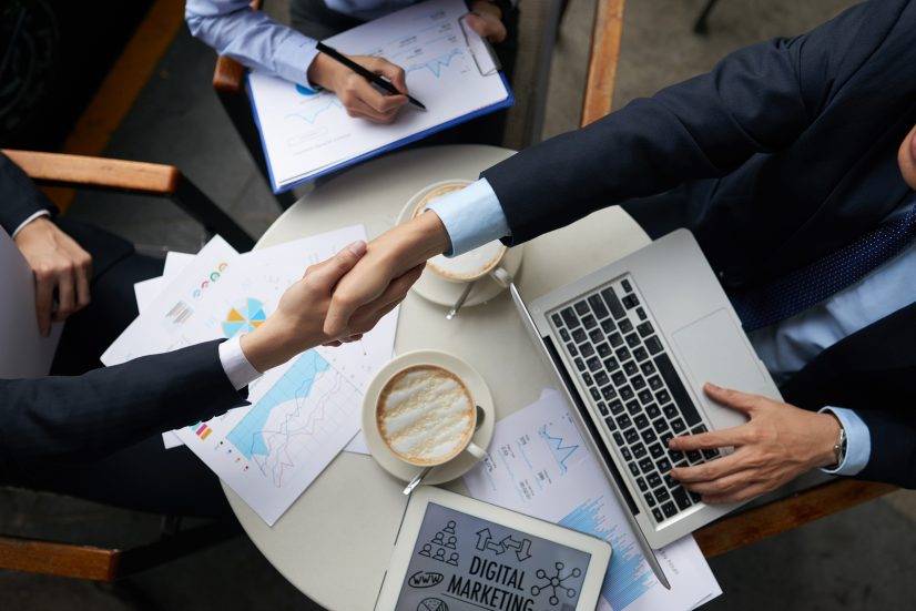 Business people shaking hands overtable with documents